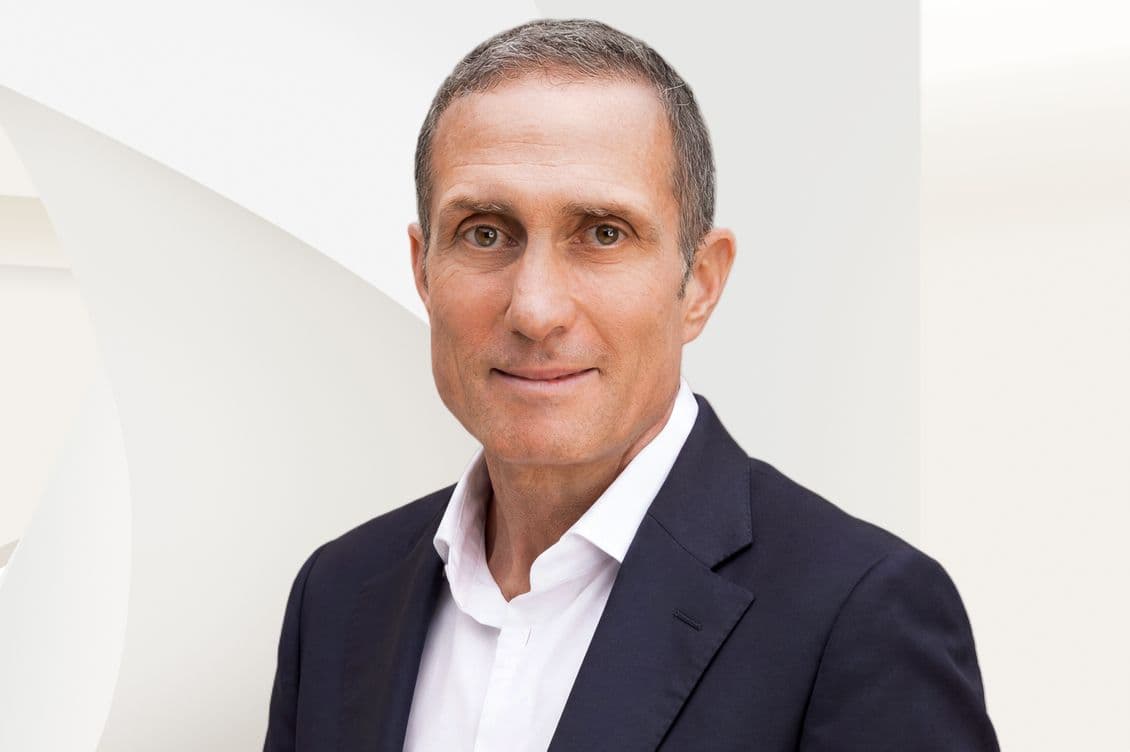 Head-and-shoulders portrait of a middle-aged man wearing a dark blazer and white shirt, neutral background, slight smile.