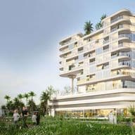 Modern, multi-story white building with curved balconies, surrounded by greenery and palm trees, people walking in the foreground.