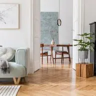 Stylish living room with a light green sofa, plants, a black piano, and a view into a dining area with a table and chairs.