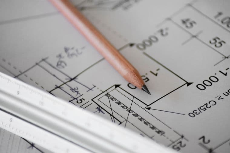 Close-up view of an architectural drawing with measurements and dimensions, showing a wooden pencil and metal ruler on the technical plan