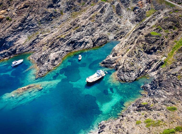 Turquoise blue sea with a rugged coastline and three boats in the coves of Empuriabrava.