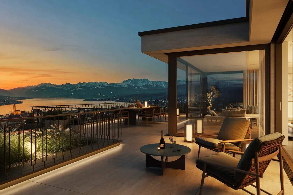 Terrace with modern lounge seating and glass walls, overlooking a lake and snow-capped mountains at sunset; warm interior glow. Immagine generata dall'intelligenza artificiale