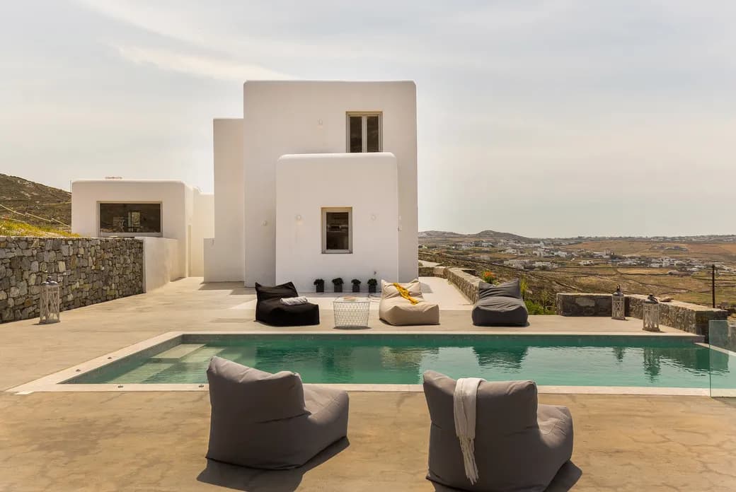 Luxusvilla mit Pool und Sitzsäcken. Weißes Gebäude mit Fenstern und Blick auf die Landschaft.