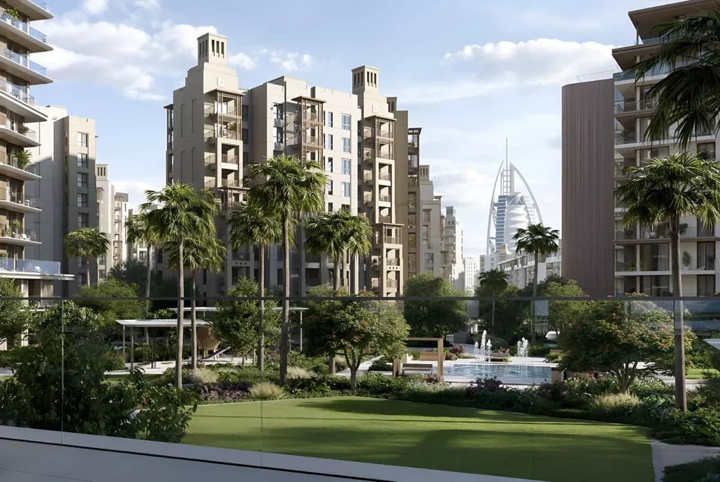 Modern urban landscape with tall buildings, lush greenery, palm trees, and a distant view of a sail-shaped skyscraper under a partly cloudy sky.
