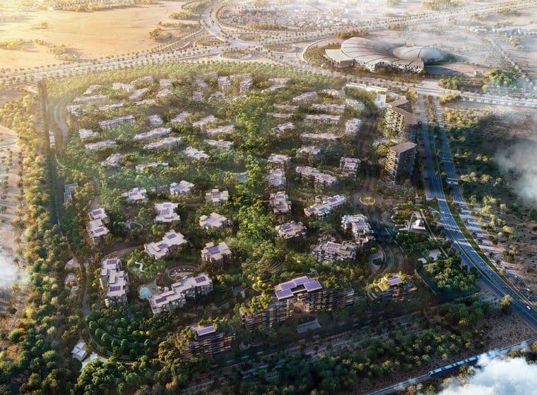 Aerial view of a lush residential area with numerous villas, surrounded by greenery, roads, and a large building complex in the distance.