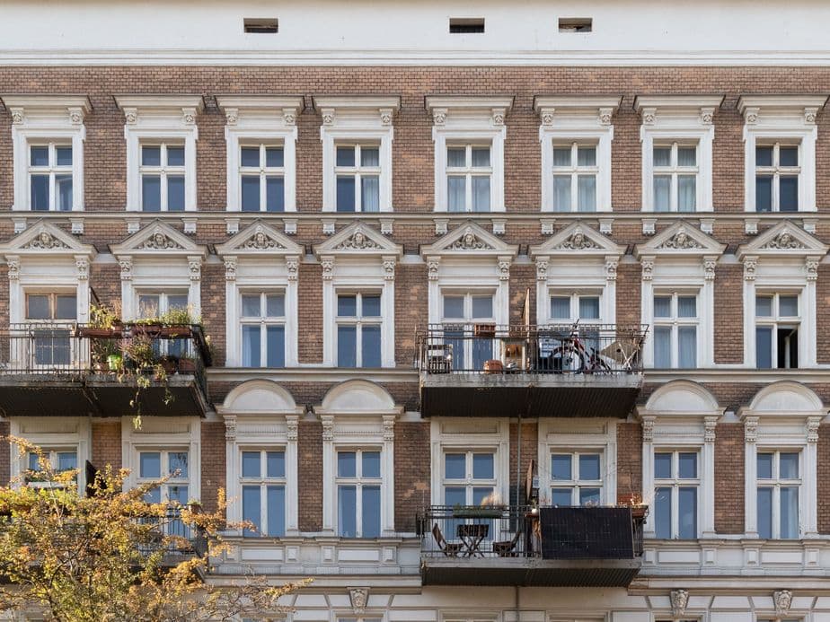 Facade of a historic building with multiple windows and three balconies, some with plants and furniture, under a clear sky.