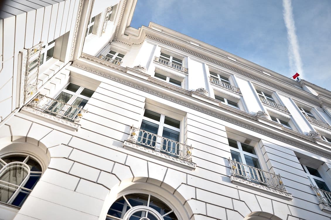 Low angle view of a white building with ornate windows and a red flag on top against a blue sky.
