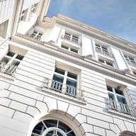 Low angle view of a white building with ornate windows and a red flag on top against a blue sky.