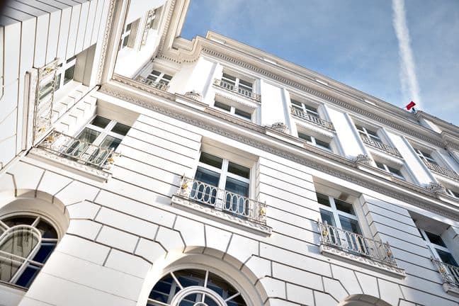 Low-angle view of an elegant white building facade featuring arched windows, ornate balconies, decorative cornices, and classical architectural details against a blue sky