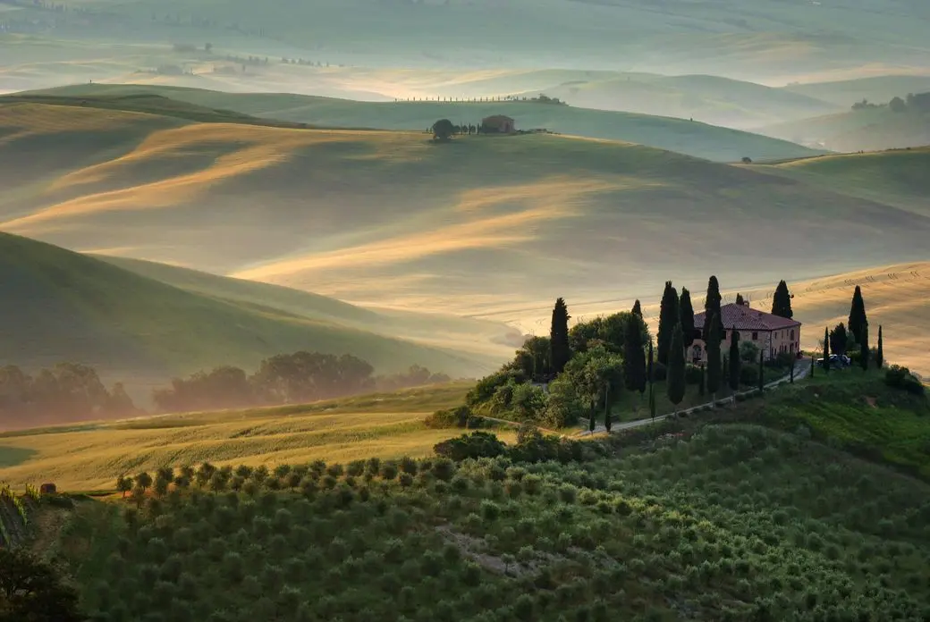 Rolling green hills with a Tuscan villa on a hilltop, surrounded by tall cypress trees and bathed in soft, golden light.