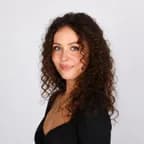 Portrait of a woman with long, curly brown hair wearing a black top, smiling gently at the camera.