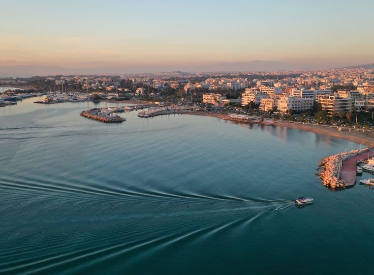 Aerial view of a boat moving on blue water near a city at sunset.