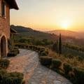 Sunset over a scenic Italian landscape with a stone house, winding path, bushes, and distant hills bathed in warm light.