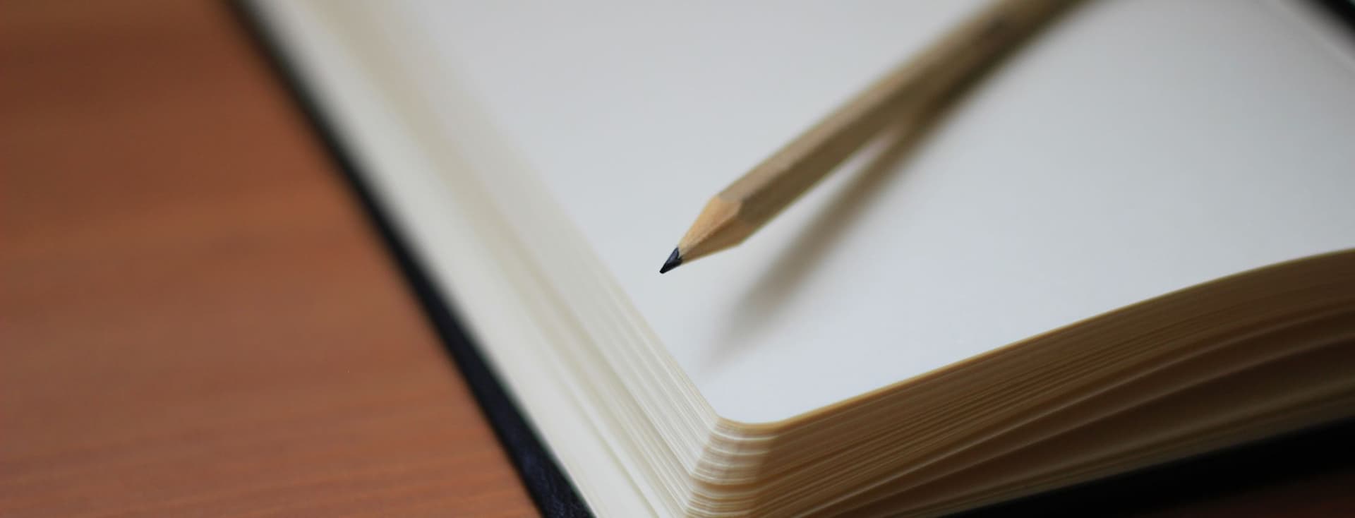Caderno aberto com páginas em branco e um lápis sobre uma mesa de madeira.