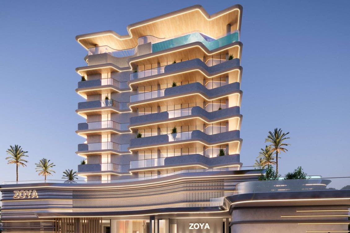 Contemporary multi-story building with curved balconies, illuminated at dusk, featuring palm trees and a sleek, modern design.