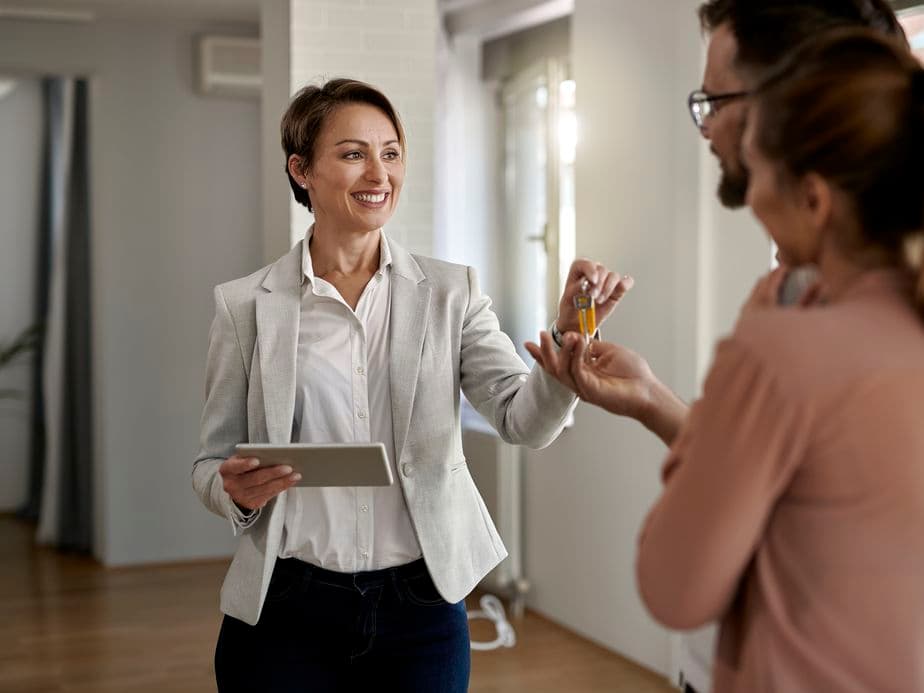 Young happy real estate agent giving house keys to a couple who is buying a new home.