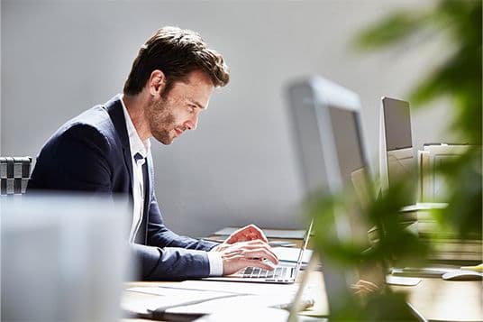 Ένας επαγγελματίας εργάζεται στον υπολογιστή του, πιθανόν εξετάζοντας στοιχεία αγοράς ή προετοιμάζοντας προτάσεις για πελάτες.