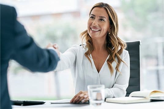 Μια επαγγελματίας χαιρετά έναν πελάτη με χειραψία, πιθανόν μετά από μια επιτυχημένη συμφωνία ή πρώτη συνάντηση.