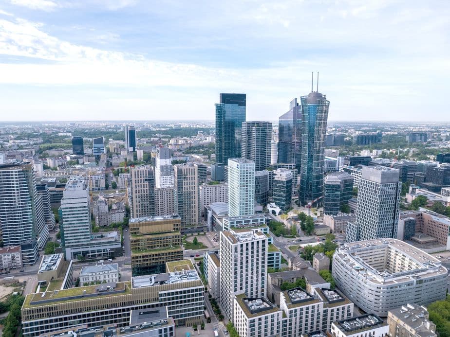 Aerial view of a modern cityscape with tall skyscrapers and diverse buildings under a blue sky.