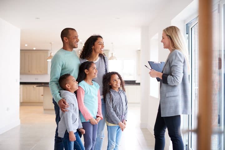 A real estate agent shows a young family their new home. The family is smiling and looking around the bright, white room.