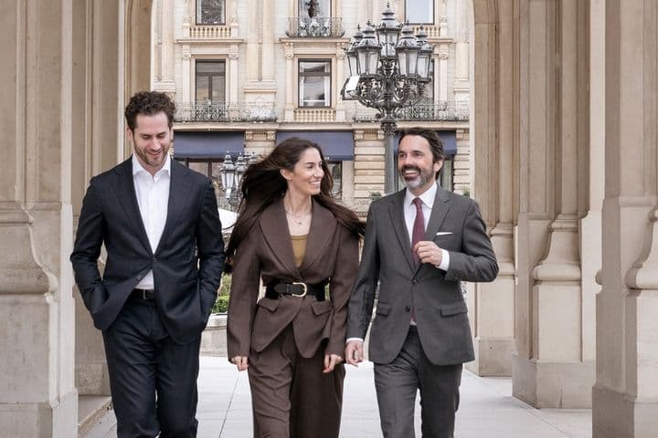 Drei Menschen gehen sich unterhaltend durch einen Bogengang, im Hintergrund ist ein Altbau-Mehrfamilienhaus zu sehen