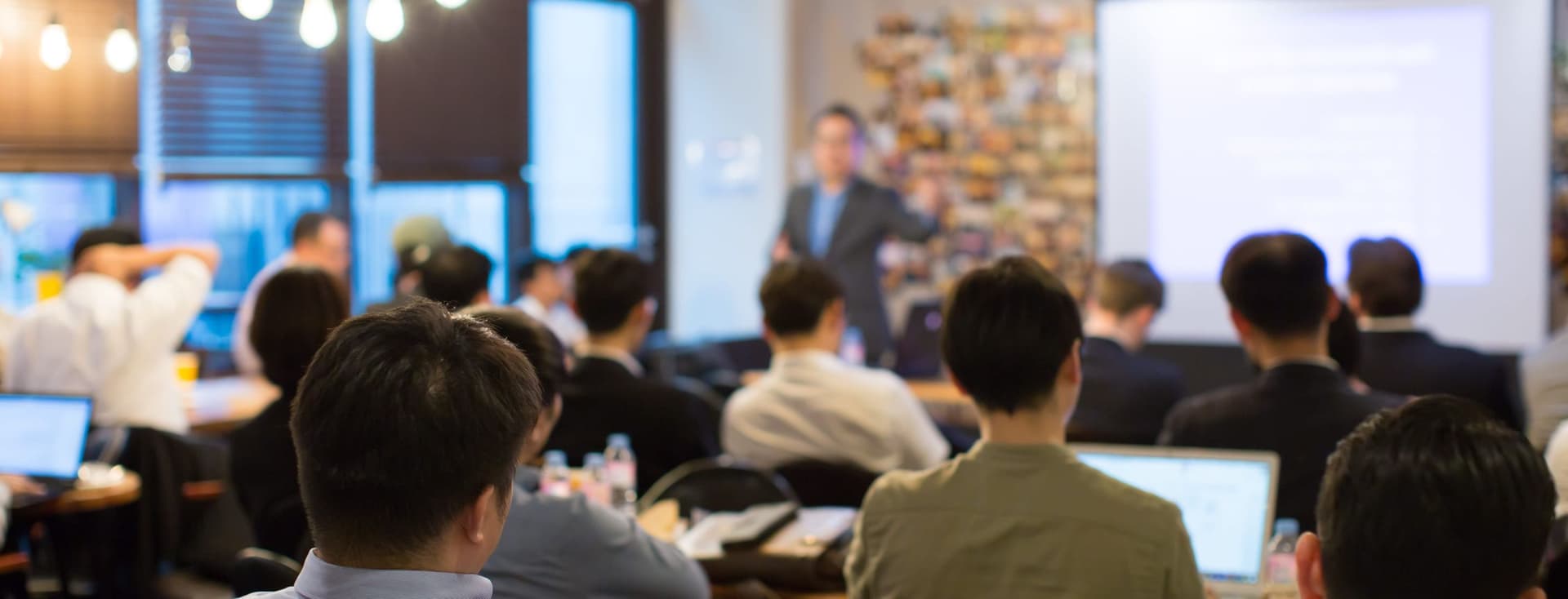 Le public écoute un orateur lors d'une conférence immobilière. Un écran de projection se trouve à l'arrière-plan.