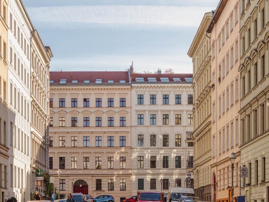 Street view of European-style buildings with ornate facades and parked cars under a clear blue sky.