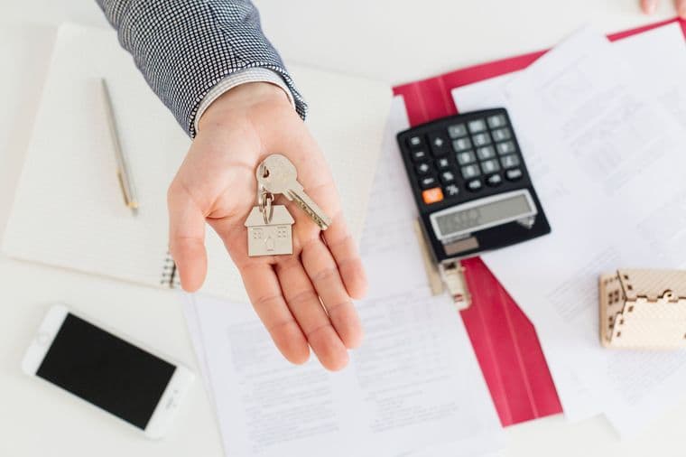 Fogli con numeri e calcoli fiscali accanto a una calcolatrice e alle chiavi di casa, a rappresentare i costi e le tasse legati all’acquisto di una seconda casa.