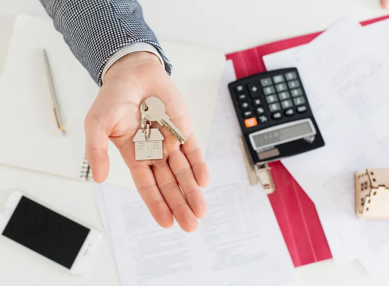 Sheets with numbers and tax calculations next to a calculator and house keys, representing the costs and taxes associated with the purchase of a second home.