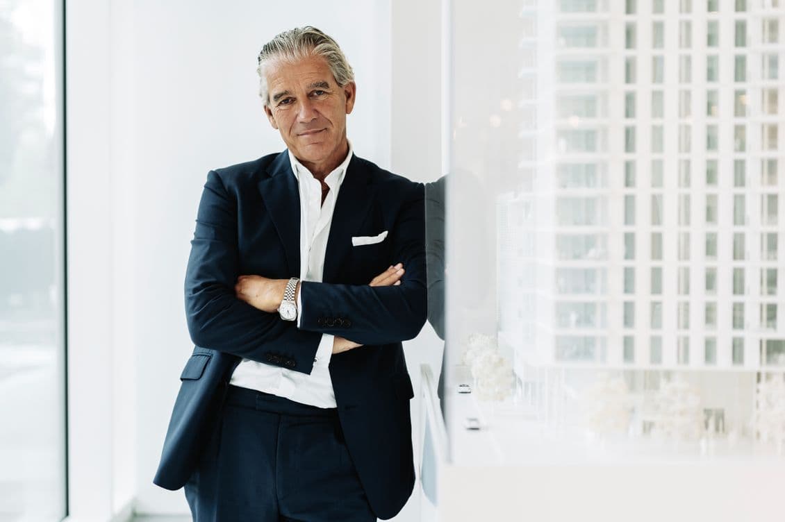 Professional businessman in dark navy suit and white shirt standing confidently with arms crossed against modern office building background with glass windows