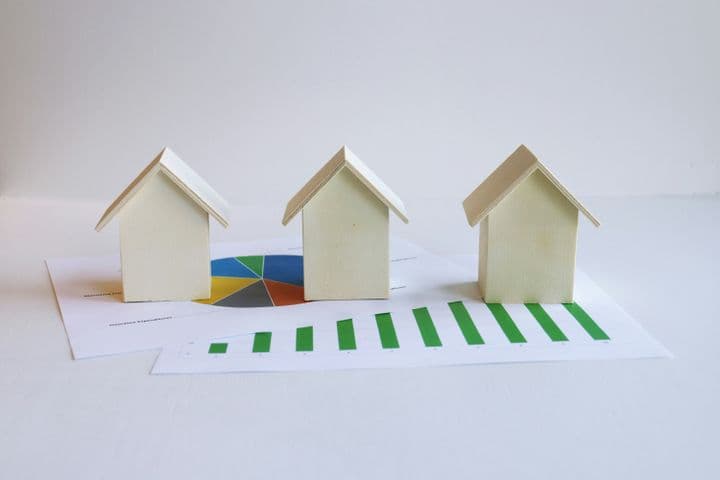 "Image showing several small wooden houses placed over printed financial or statistical charts."