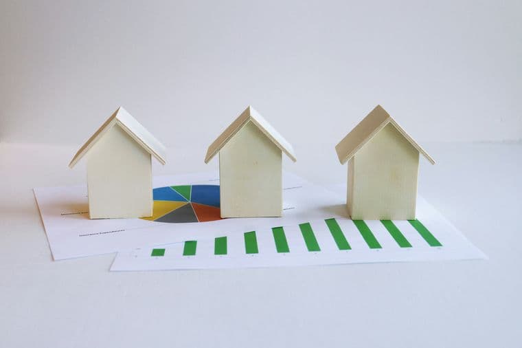 "Image showing several small wooden houses placed over printed financial or statistical charts."