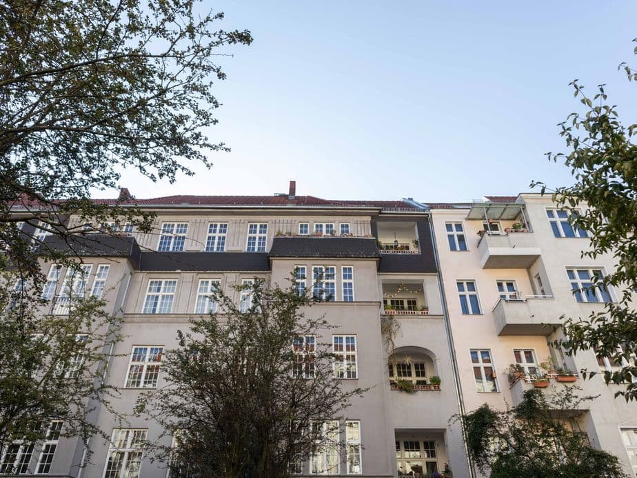 View of a residential building with multiple floors, balconies, and trees in the foreground under a clear sky.