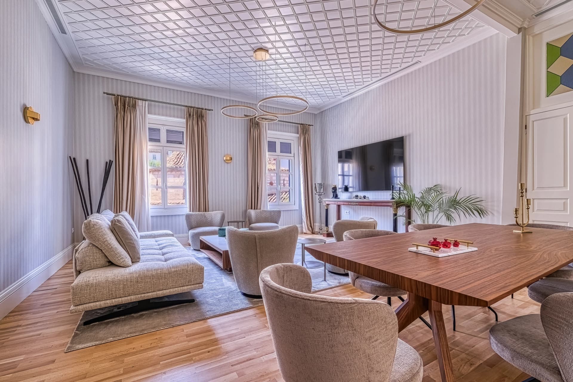 Elegant living and dining room featuring light hardwood floors, textured wallpaper, modern rounded armchairs, and a large wooden dining table.