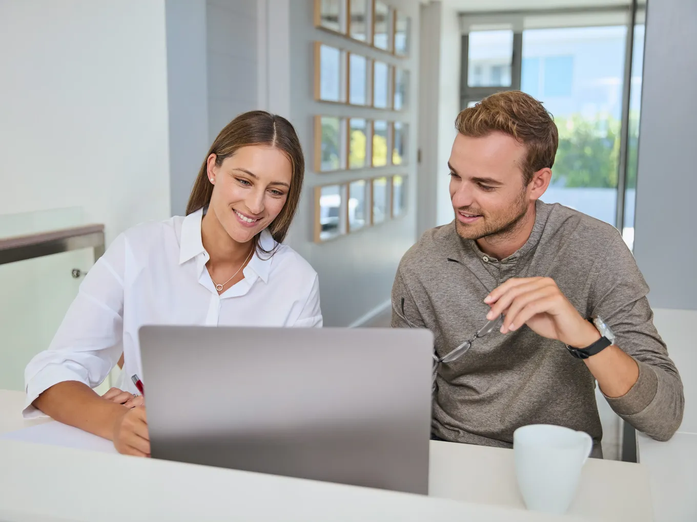 Young couple sitting together at a table, smiling as they look at a laptop, clearly engaged in a consultation or research.