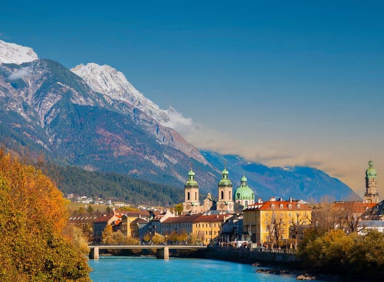 Autumnal view of Innsbruck with the Inn river, colorful trees and the Nordkette mountain range in the background