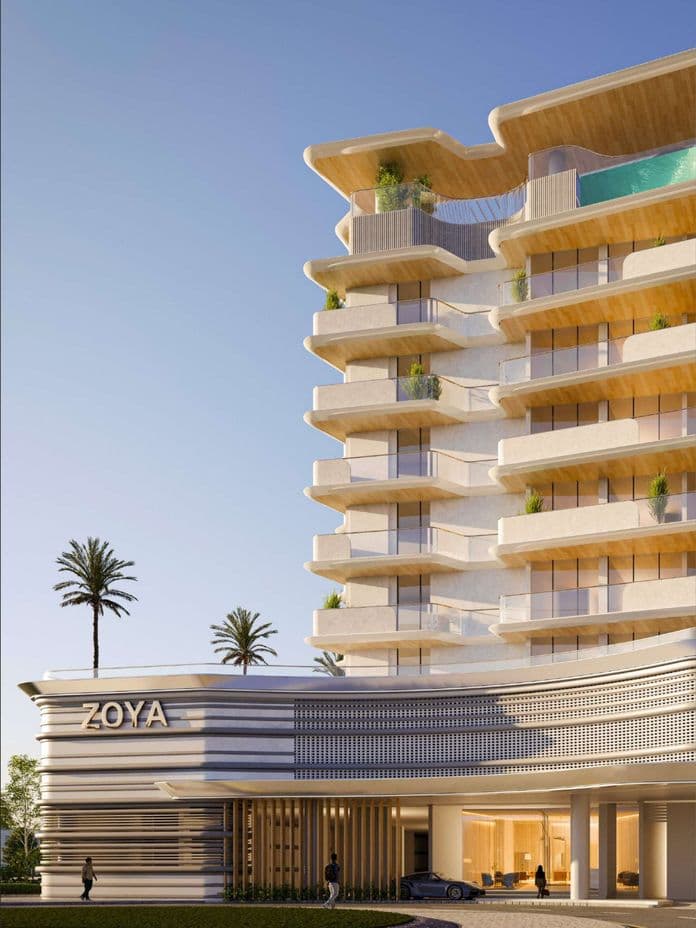 Modern multi-story building with balconies, labeled "ZOYA," under a clear sky. Palm trees and a few people are visible nearby.