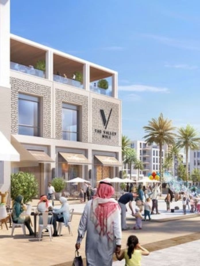 Outdoor pedestrian plaza with cafes, shops, and people walking. Palm trees line the area under a clear blue sky.