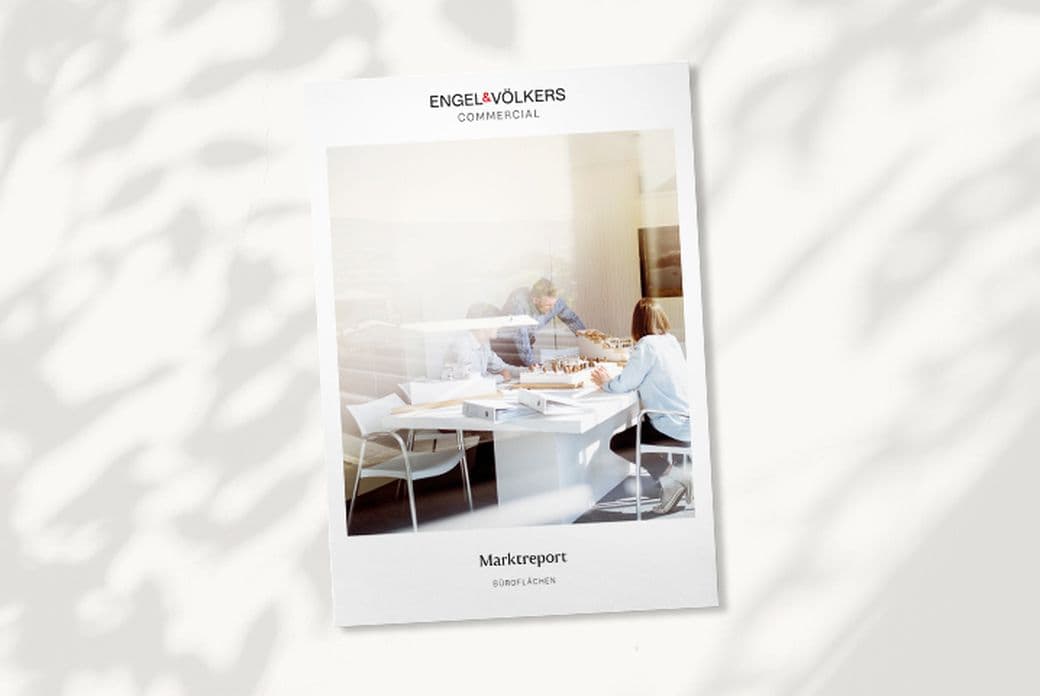 White booklet titled "Marktreport" by Engel & Völkers, showing people at a conference table, with tree shadows on the surface.
