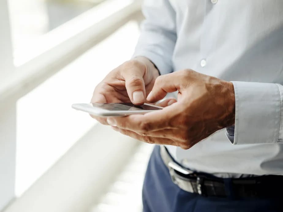Close-up of business professional's hands in white shirt sleeve using smartphone, photographed against bright white background in modern office environment