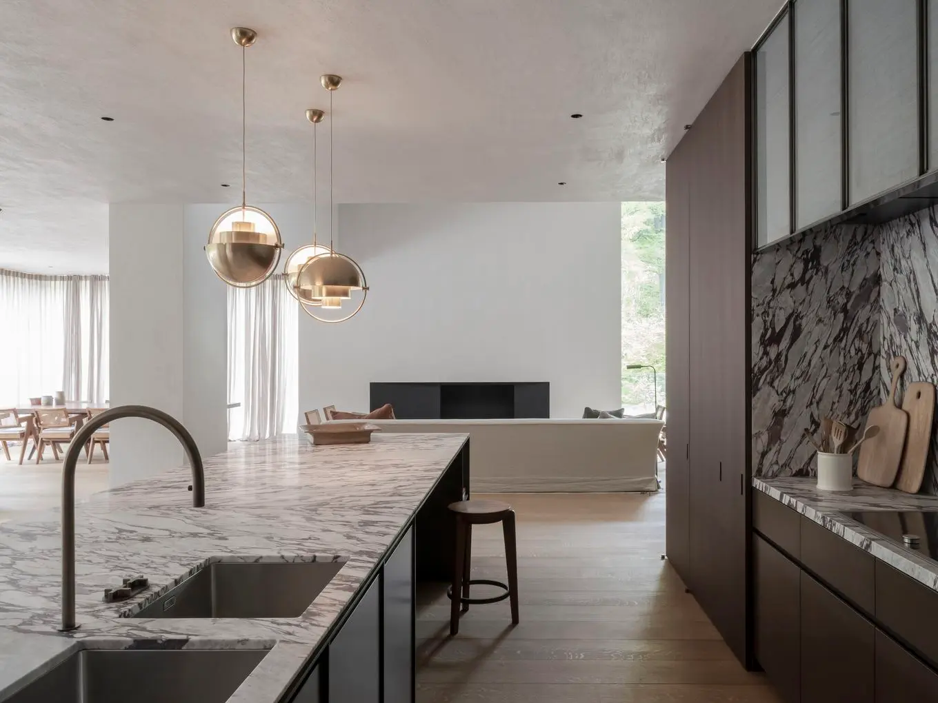 Open-concept kitchen with marble island, brass pendant lights, and a view into the living room with a large window.