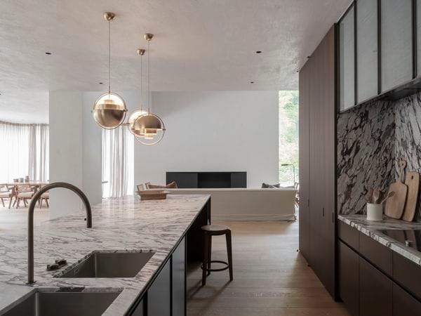 Cuisine à aire ouverte avec îlot en marbre, suspensions en laiton et vue sur le salon avec une grande fenêtre.