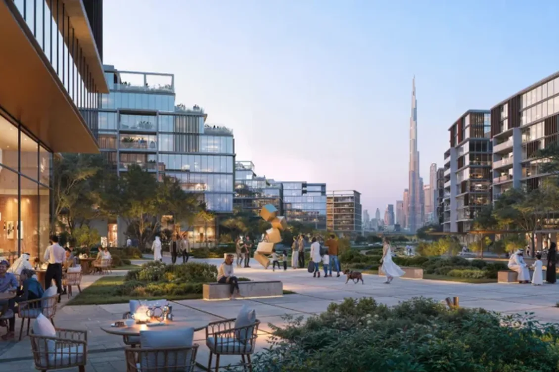 Modern urban courtyard with people socializing, dining, and walking dogs. Surrounding glass buildings and distant skyline at twilight.