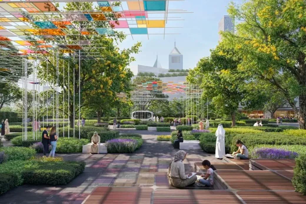 A park scene with people relaxing, surrounded by greenery and vibrant, colorful canopy structures overhead. City buildings are visible in the background.