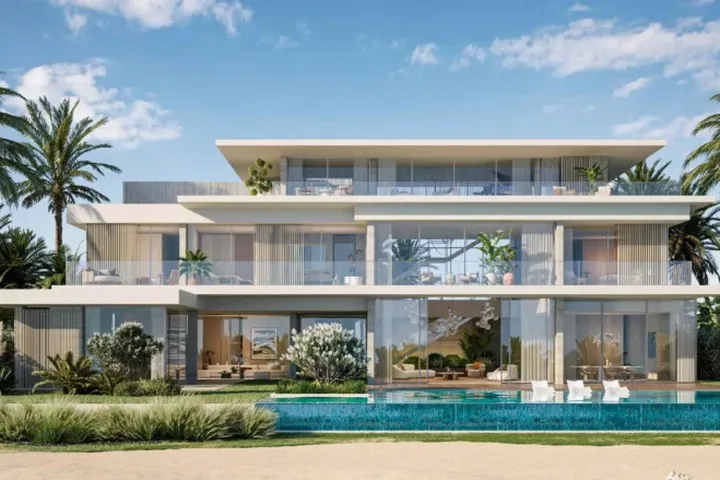 Modern three-story beachfront villa with large glass windows, surrounded by palm trees and a pool, under a blue sky with clouds.