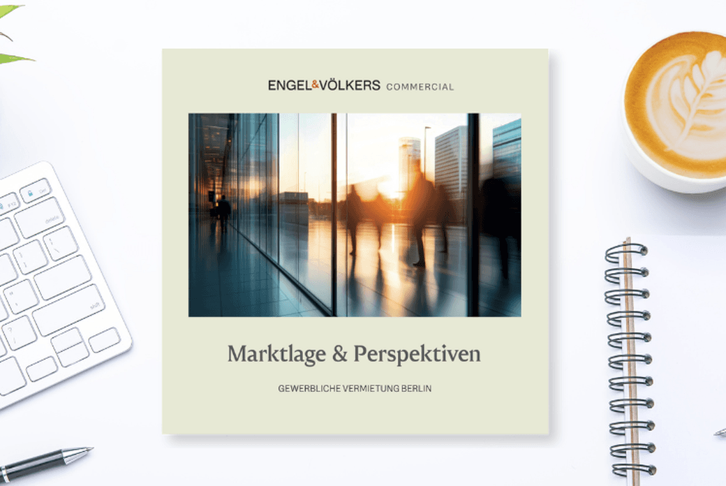 Coffee, notebook, keyboard, and a brochure titled "Marktlage & Perspektiven" with a blurred cityscape image on a white desk.