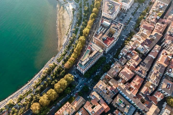 Vue aérienne d'une ville côtière avec une plage, une promenade, des arbres, des bâtiments et des rues.