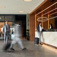 Exklusive Hotellobby mit Marmor-Rezeption, moderner LED-Beleuchtung und geschäftigen Geschäftsreisenden, ausgestattet mit zeitgenössischen Designelementen aus Holz und Stein und stimmungsvoller Beleuchtung.