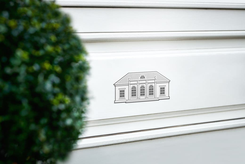 Architectural line illustration of a classical villa facade with arched windows mounted on a white wall, partially framed by blurred green foliage in the foreground