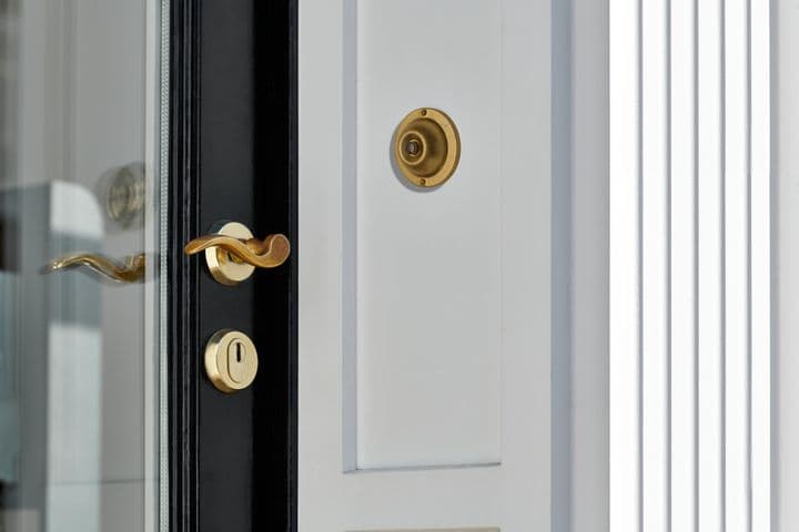 Close-up of a white door with a black frame, featuring a gold handle, lock, and doorbell.